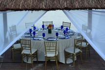 place settings on a table under a tiki hut on a beach for a dinner reception 