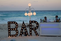 A bar sign on a beach and bartenders at a reception in Cancun