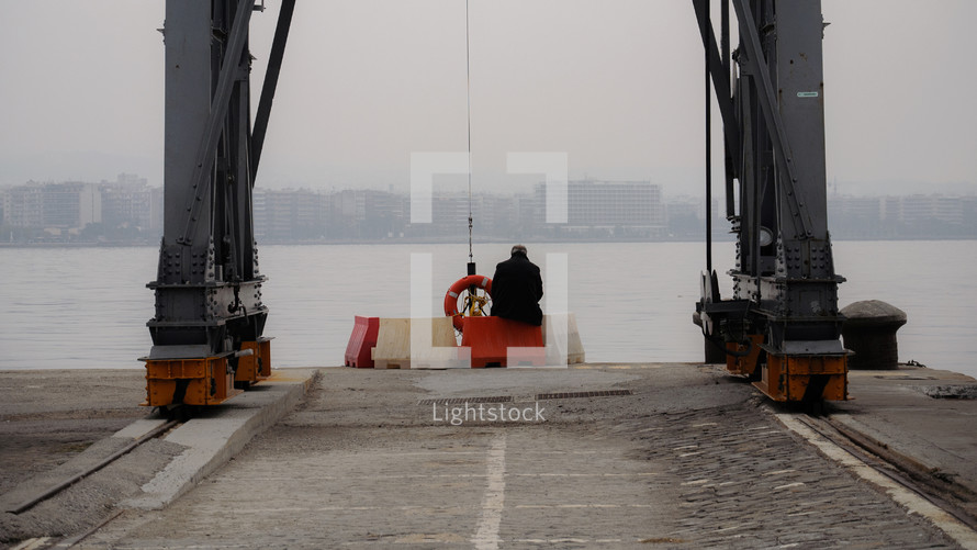 man sitting on a blockade on a dock 