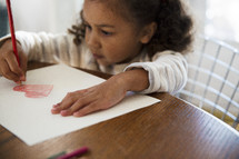 a girl child coloring a heart on paper 