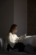 a woman sitting on a couch reading a Bible in sunlight 