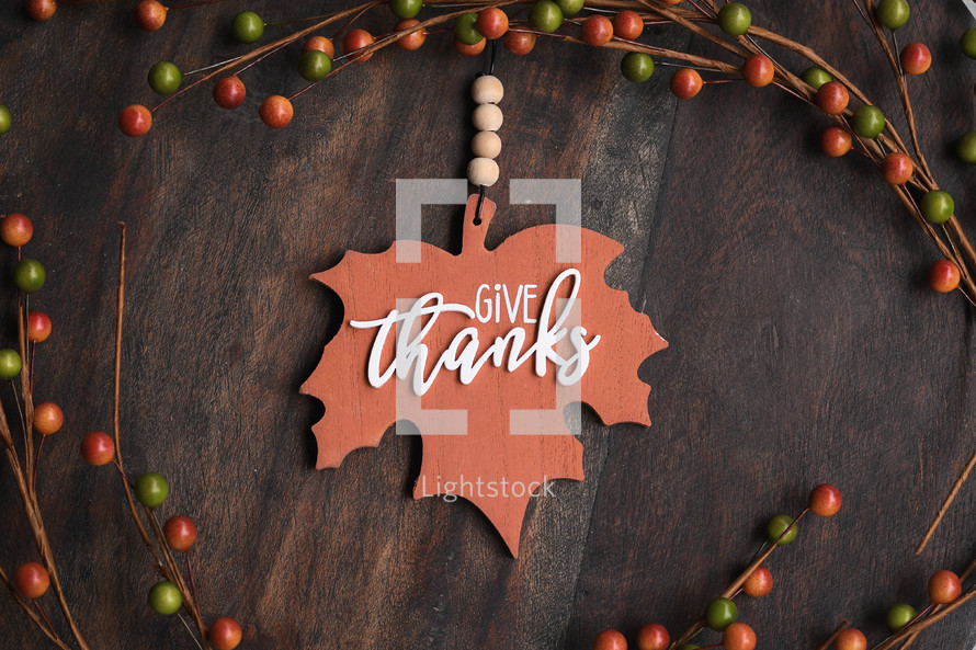 Maple leaf with the words Give Thanks surrounded by fall colors on a dark wood background