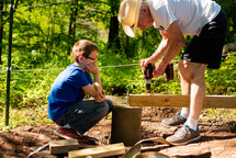 a grandson and grandfather drilling a hole into a board 