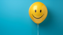 Smiley face on a yellow helium balloon with a blue background. 