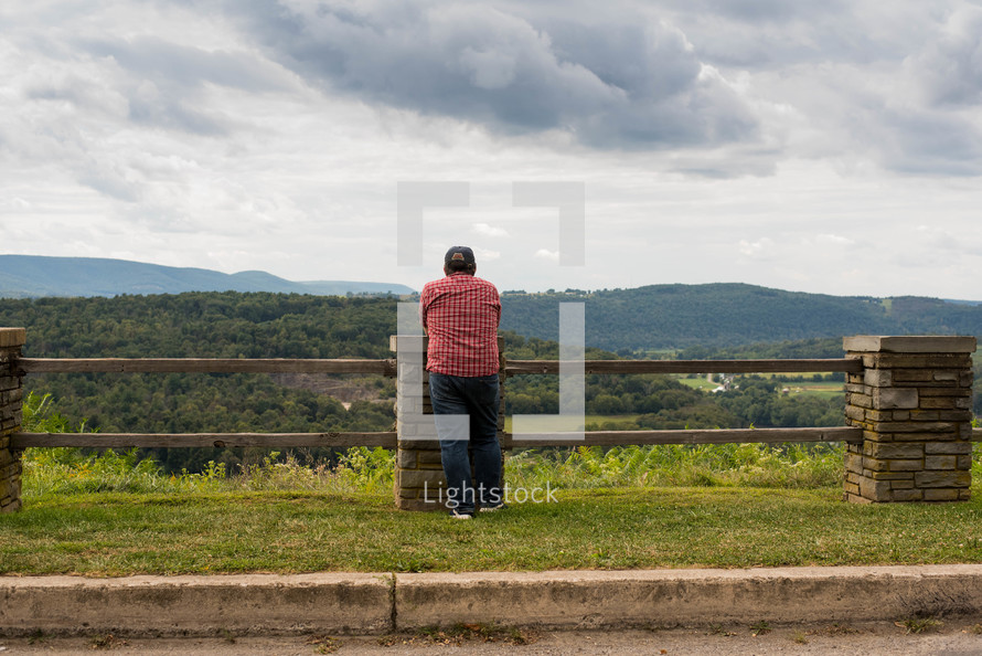man looking over a fence at green landscape 