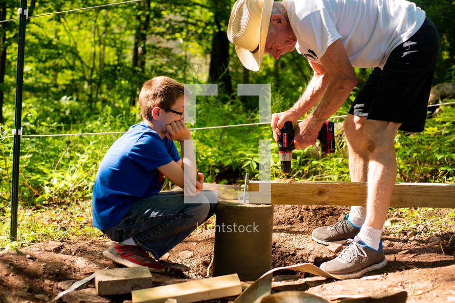 a grandson and grandfather drilling a hole into a board 