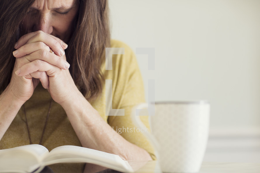 a woman praying over a Bible sitting at a kitchen table 