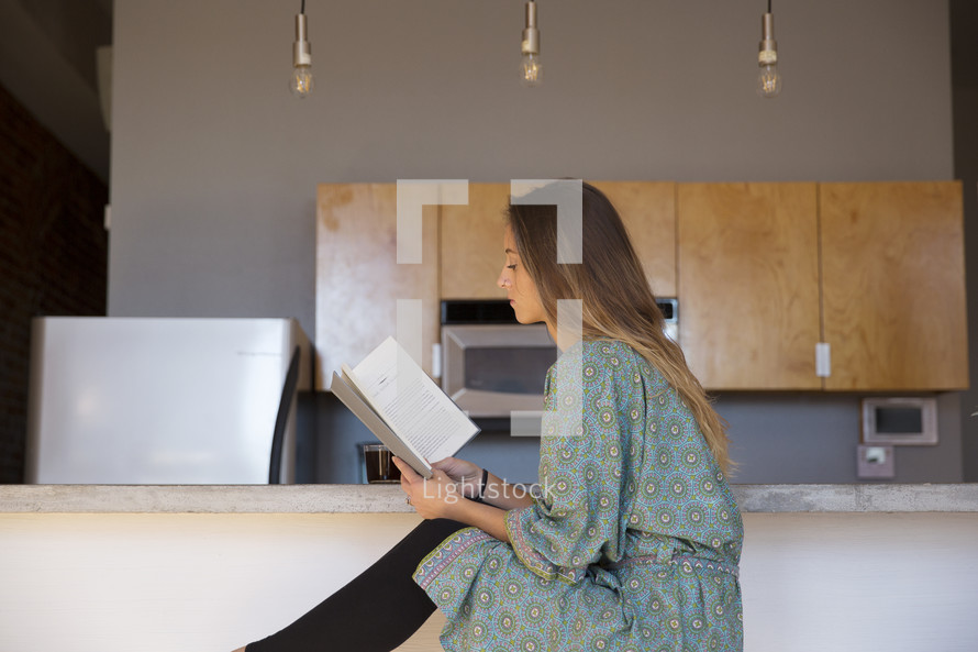 a woman in her pajamas reading in the kitchen with coffee 