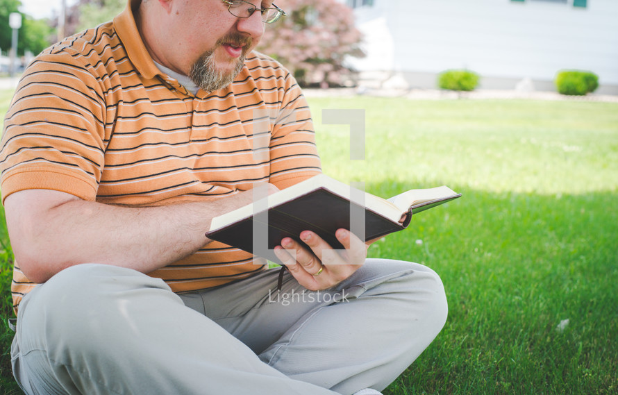 a man sitting in the grass reading a Bible  in the sunlight