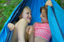 A little boy and girl playing in a blue hammock.