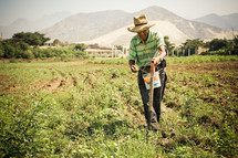 Old man planting seeds in a field, mountains in the background