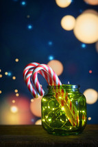 Candy canes and twinkle lights in a green jar with whimsical background