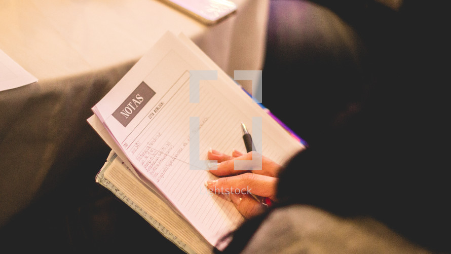 a woman taking notes in a notebook at a conference 