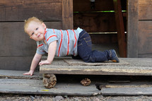 A baby boy crawling on a rustic wood porch.