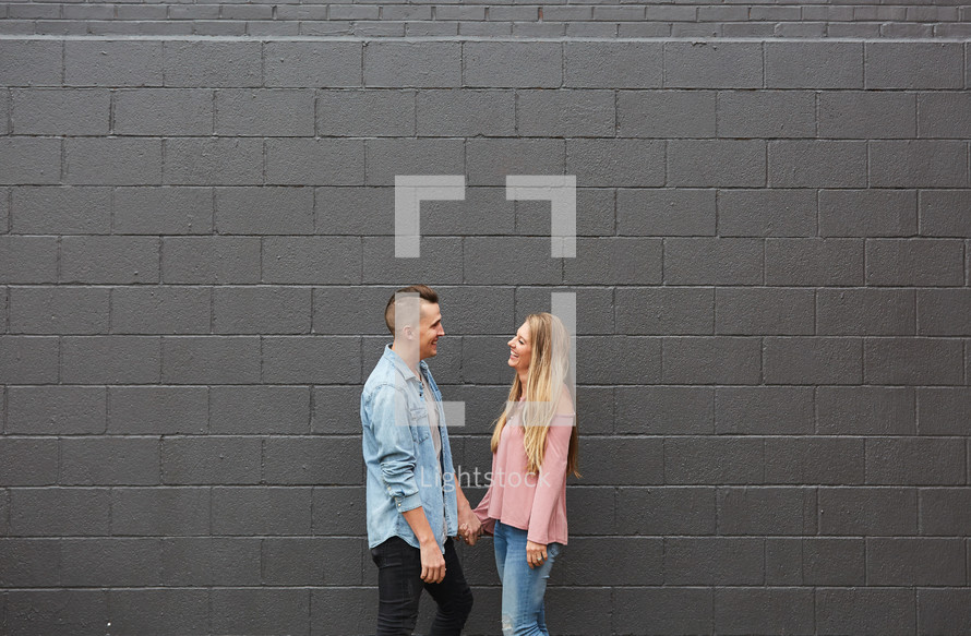 a couple walking holding hands in front of a gray wall 
