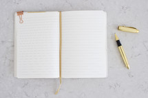 An open blank notebook and a gold pen.