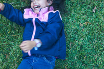 a little girl in a jacket rolling in the grass 