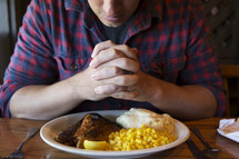 man with praying hands over a plate before a meal 