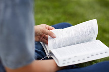 man sitting in the grass reading a Bible 