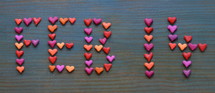 The date FEB 14 for February 14th written with many little colorful clay hearts on cyan wooden background 