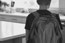 a middle school student with a backpack standing in a kitchen ready for school 