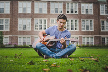 man sitting in grass playing a guitar 