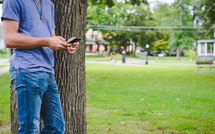 man standing beside of a tree texting 