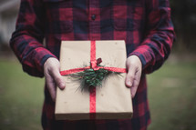 A man holding a gift wrapped in brown paper and red ribbon