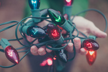 A woman holding a tangle of multi-colored Christmas lights.