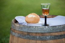 A glass of wine and a bread roll, sitting on a wine barrel