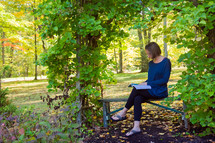 a woman sitting on a bench doing her devotions with a Bible outdoors 