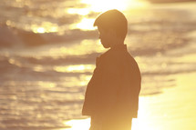 silhouette of a boy child standing on a shore at sunset 
