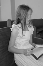 a little girl singing from a hymnal in a church pew 