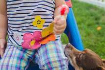 a toddler girl holding a sucker and a dog looking up 