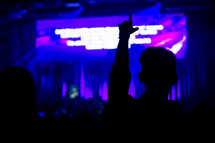 silhouette of a person with a raised hand at a worship service 