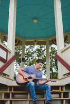 A young man plays a guitar outside.