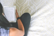 young woman reading a Bible on a a tablet in bed 