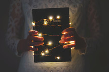 a woman holding a Bible wrapped in fairy lights 