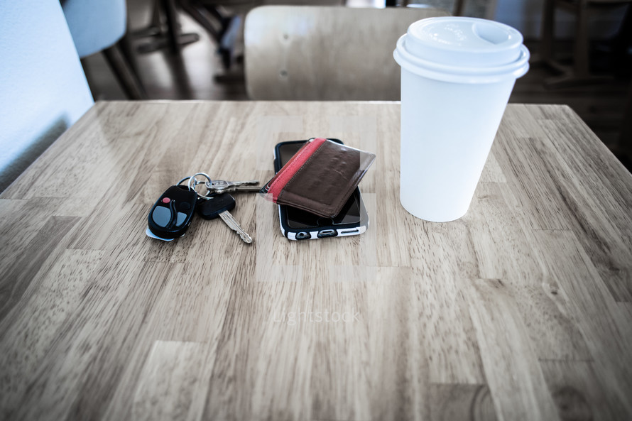 car keys, cellphone, wallet, and coffee cup on a cafe table 