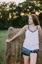 a teen girl standing in front of a hay bale