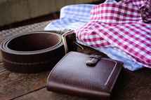 leather belt and wallet and folded collared shirts 