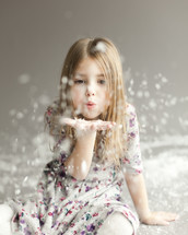 A joyful little girl blowing snow off her hand on grey backdrop