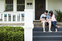 Young mom and dad sitting on the front steps of a house with their son.