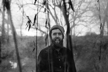 man with a beard and wool cap standing in the woods 