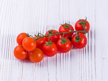 Branch of fresh fragrant cherry tomatoes isolated on white wooden table.