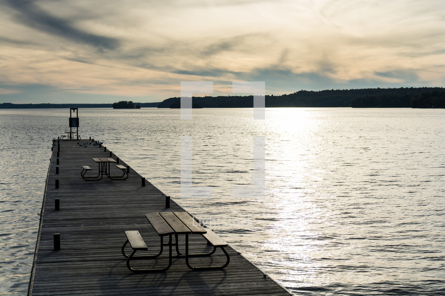 Picnic tables on a wooden pier on a lake.