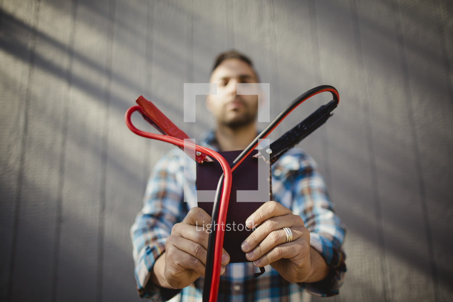 Man holding Bible with jumper cables attached to corners.
