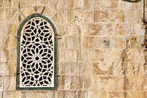 Ornate arched window grate in a stone wall.