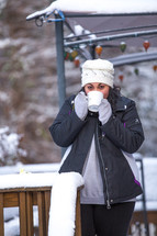 a woman standing on a snow covered deck drinking hot cocoa 