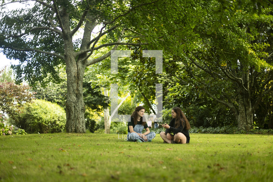 two young women sitting together talking in the grass in a beautiful setting